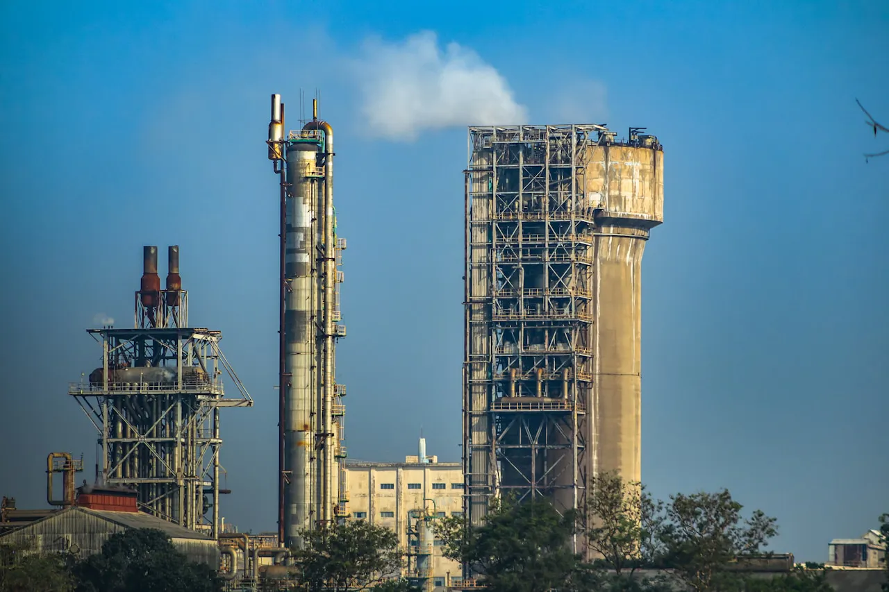 Endüstriyel gübre tesisi, üre ve amonyak depo tanklarının önünde yan yana dizilmiş tank kamyonları — Hürmüz'ün kapanışıyla beraber yükselen doğal gaz fiyatlarının fertilizör maliyetine 2027 ekimini şimdiden ipotek altına alacak şekilde geçişine gönderme